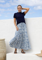Woman wearing a white based blue floral cotton skirt standing against a white wall.