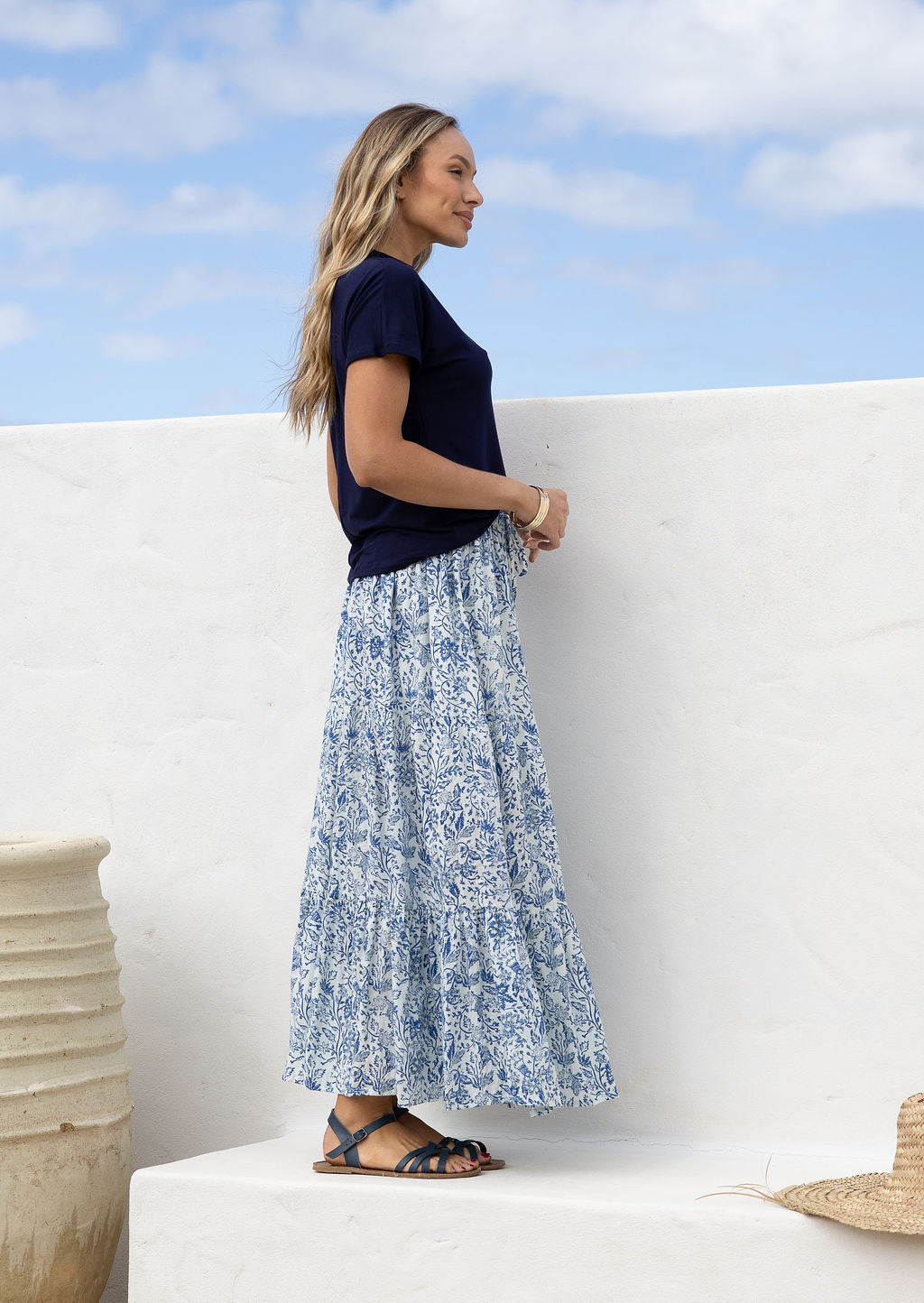 Woman wearing a white based blue floral cotton skirt standing against a white wall.