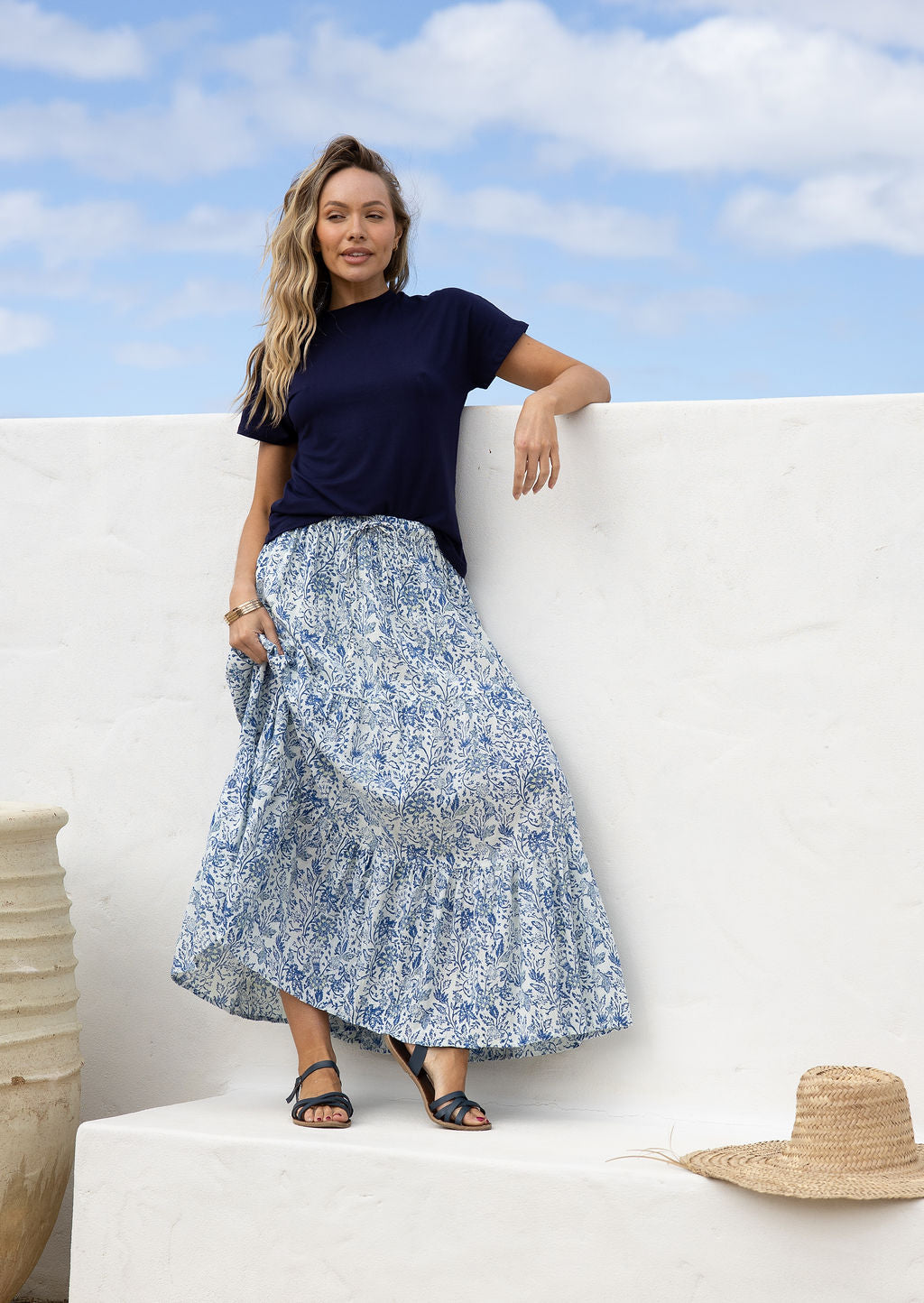 Woman wearing a white based blue floral cotton skirt standing against a white wall.
