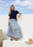 Woman wearing a white based blue floral cotton skirt standing against a white wall.