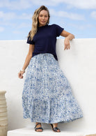 Woman wearing a 100% cotton, white based blue floral cotton skirt standing against a white wall.