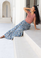Woman sitting on a ledge wearing a pink top and blue cotton floral maxi skirt in a bright, architectural setting.