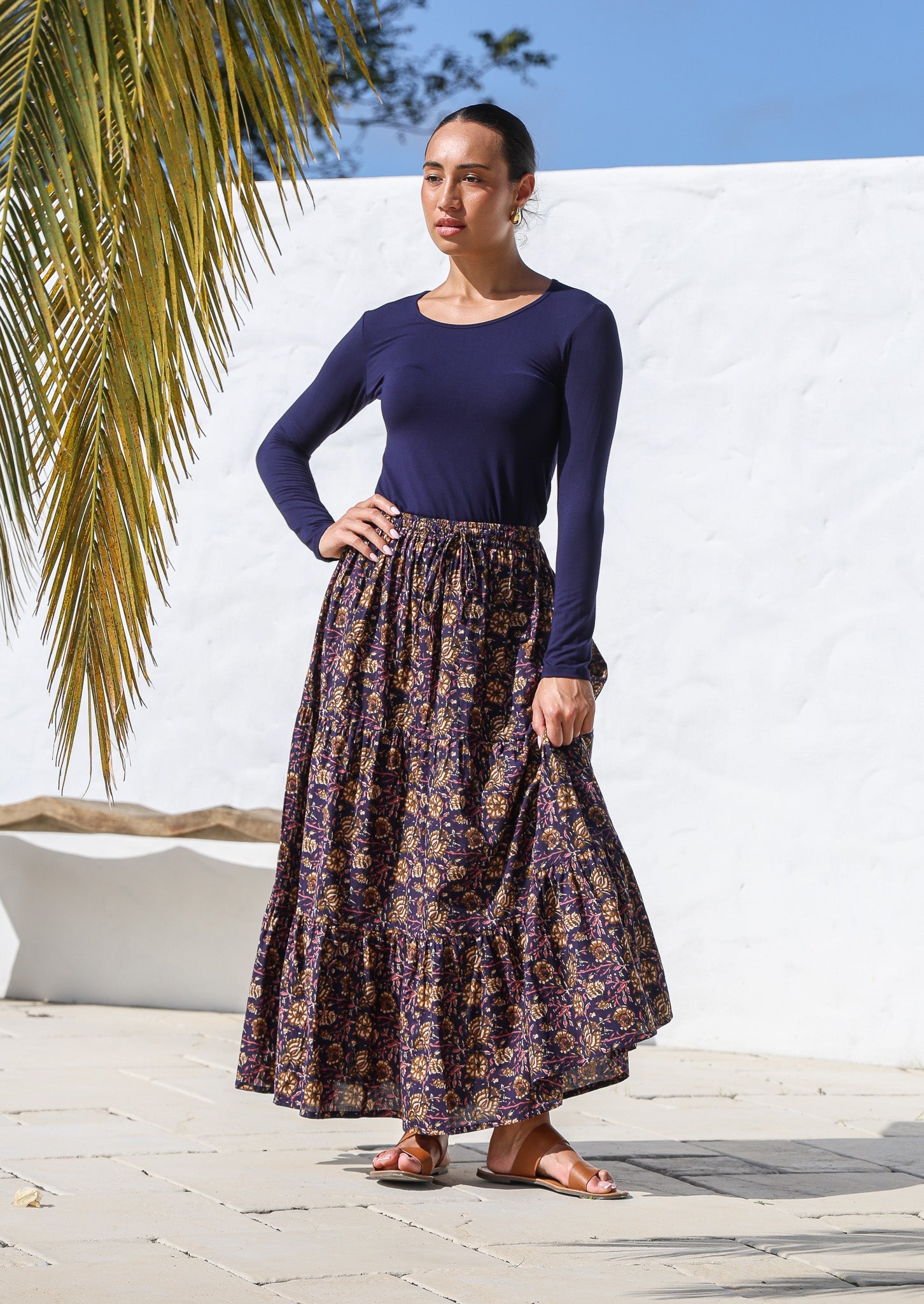 Woman stands in three tiered cotton maxi skirt in dark purple with elastic waistband, and drawstring.
