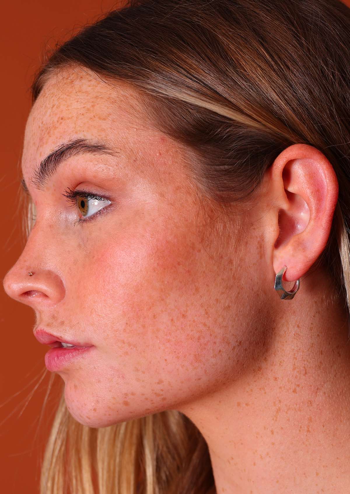 Woman wears sterling silver hollow hoop earrings with six 'sides' and subtle faceting