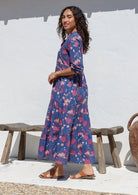 Woman stands side ways wearing a 100% cotton tiered maxi dress in navy blue with 3/4 sleeves, pockets and mandarin collar