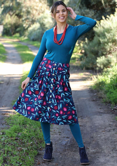 Model wears 100% cotton fruit print skirt. Skirt features box pleats, buttons, belt loops, pockets and sits under the knee.
