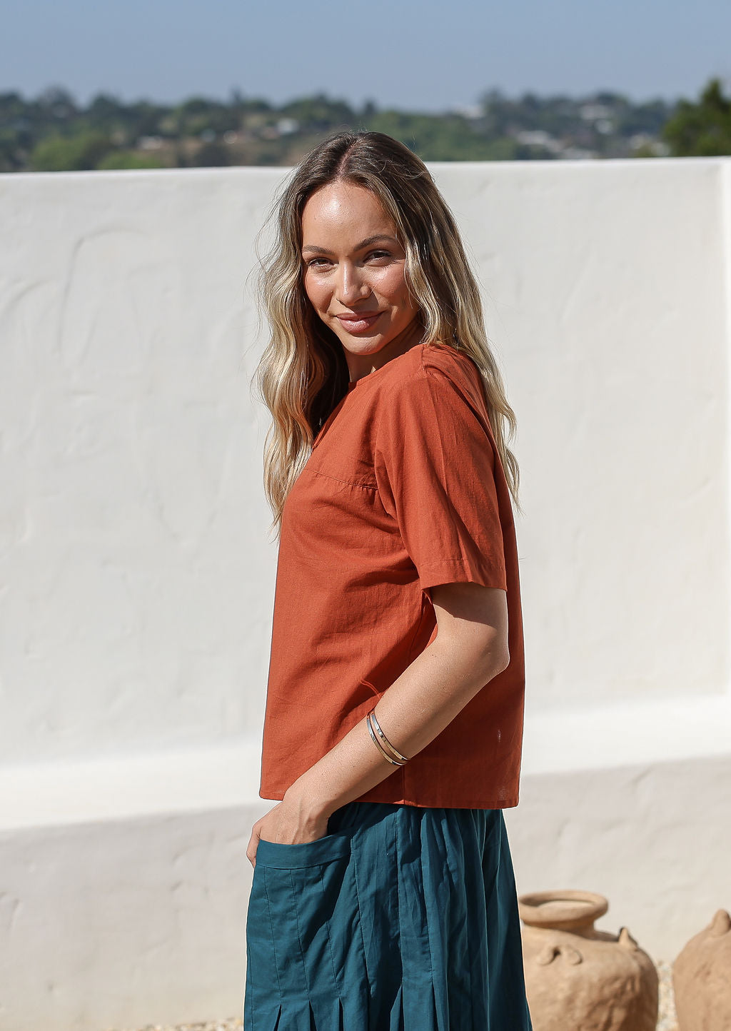 women wearing a 100% cotton rust shade top with a blue pants standing against a white background.