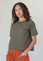 Woman wearing a rust pants and olive green shade short sleeve top standing against a white background