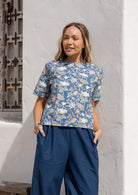 Woman wearing a loose-fit, blue floral 100% cotton boxy top with short sleeves and a seam across the bust