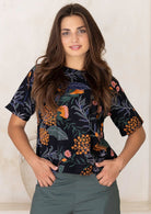 Woman wearing a 100 percent cotton, dark floral loose cut top with high round neckline and short sleeves