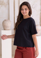 Woman standing side on in a black cotton seersucker t-shirt style top paired with rust pants