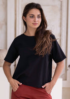 Woman wearing a black non-stretch cotton t-shirt and rust pants standing indoors.