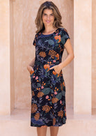 Model wears a simple knee length cotton dress with round neckline, short cap sleeves, pockets and a slight A-line skirt.