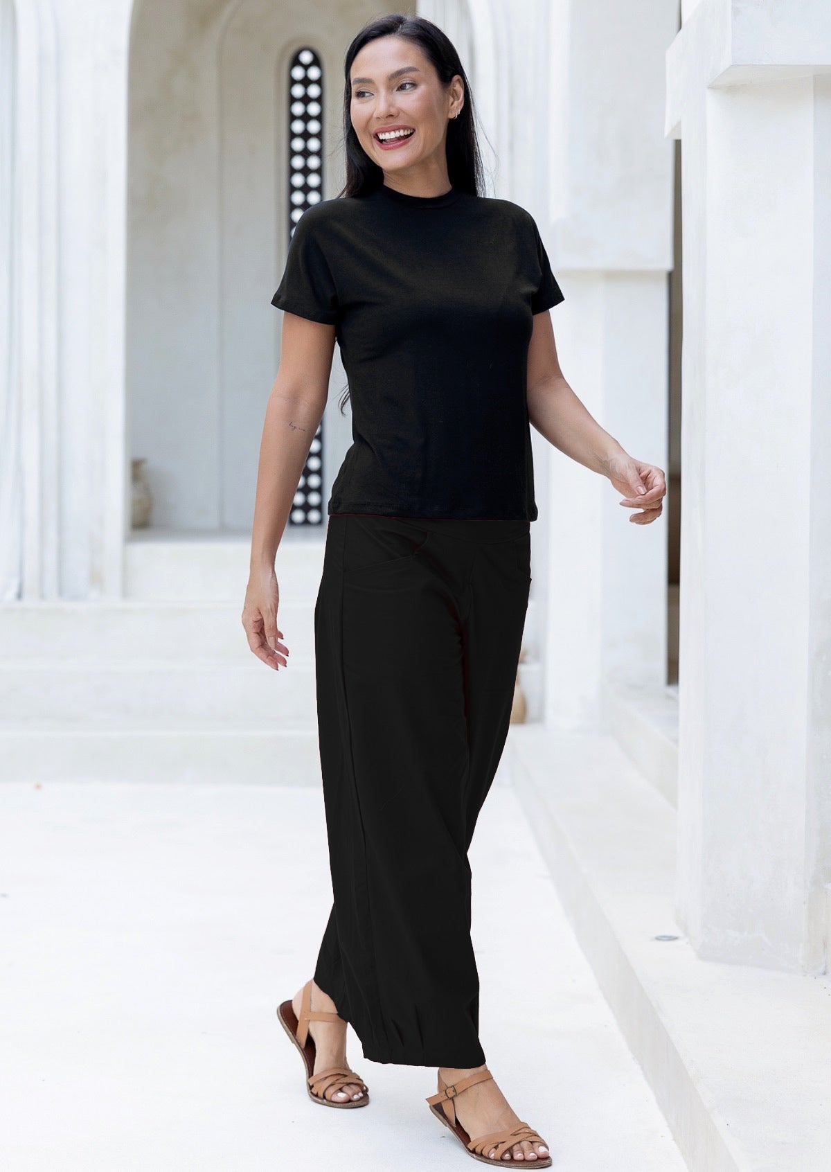 Woman wearing a black cotton pants and t-shirt standing in a bright, minimalistic setting.