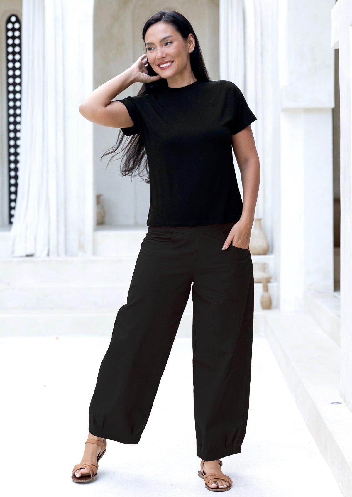 Woman wearing a black wide legged cotton pants standing in a bright, minimalistic room.