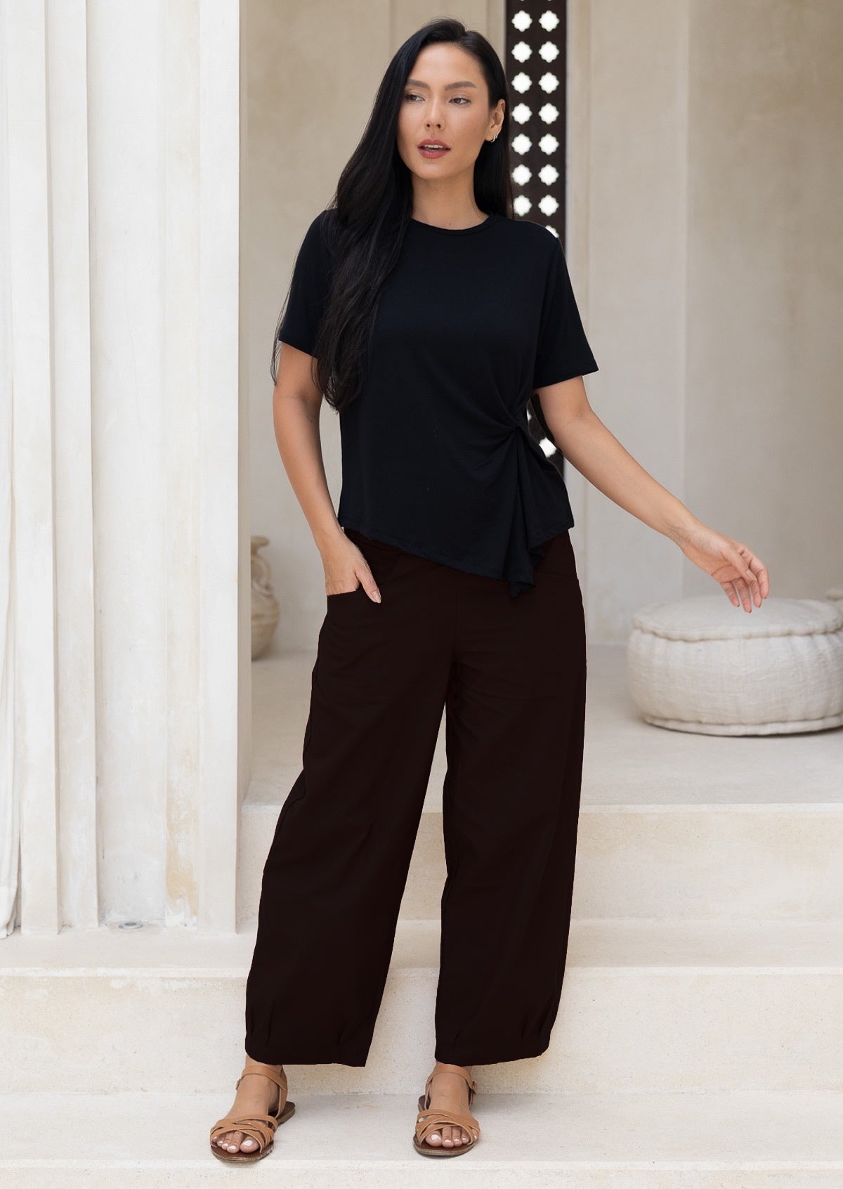 Woman wearing a black wide legged cotton pants standing 
minimalistic room.