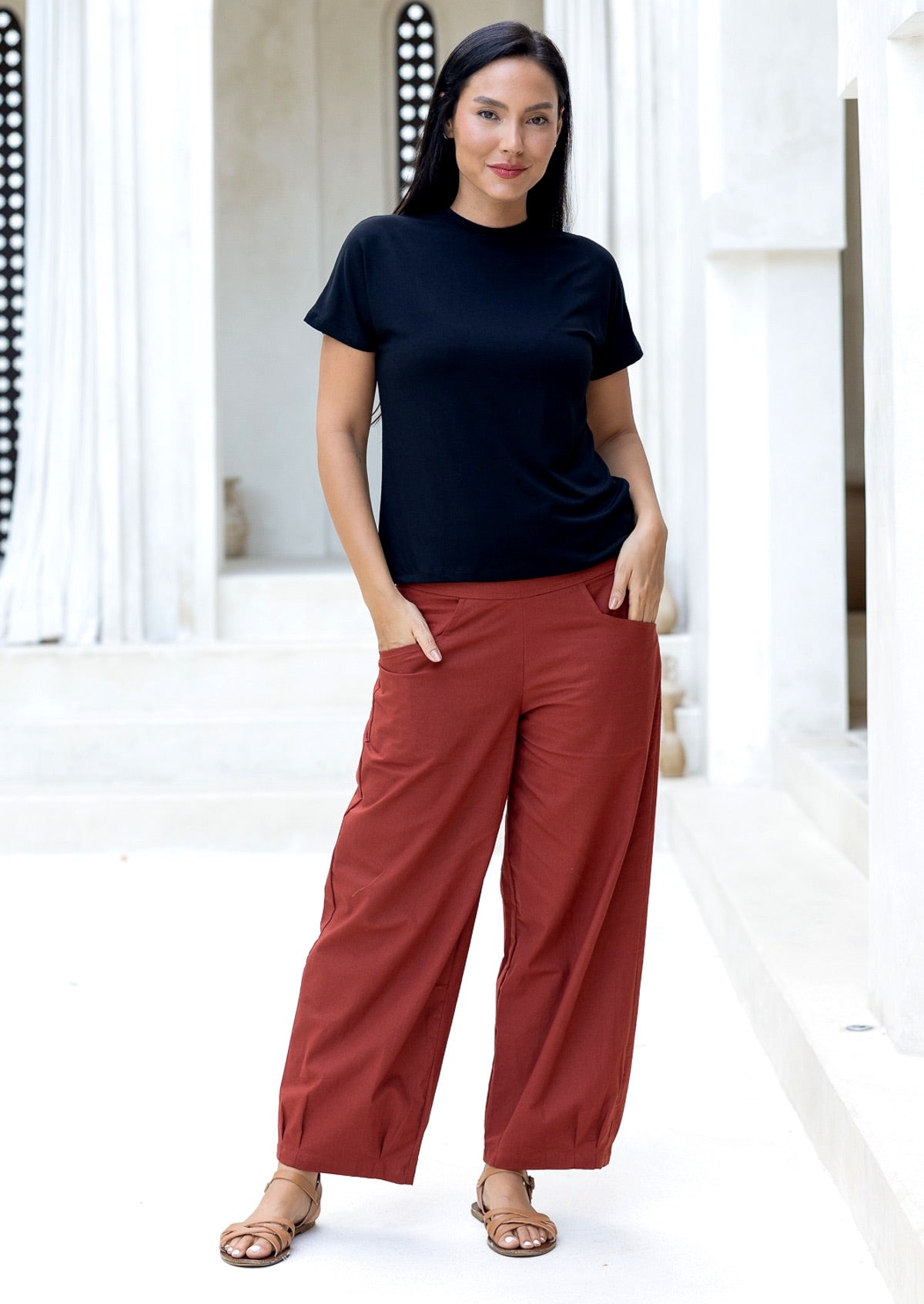Woman with hands in pocket wears 100% cotton wide leg pants in rust with tapered ankles, side zipper and pleated ankles