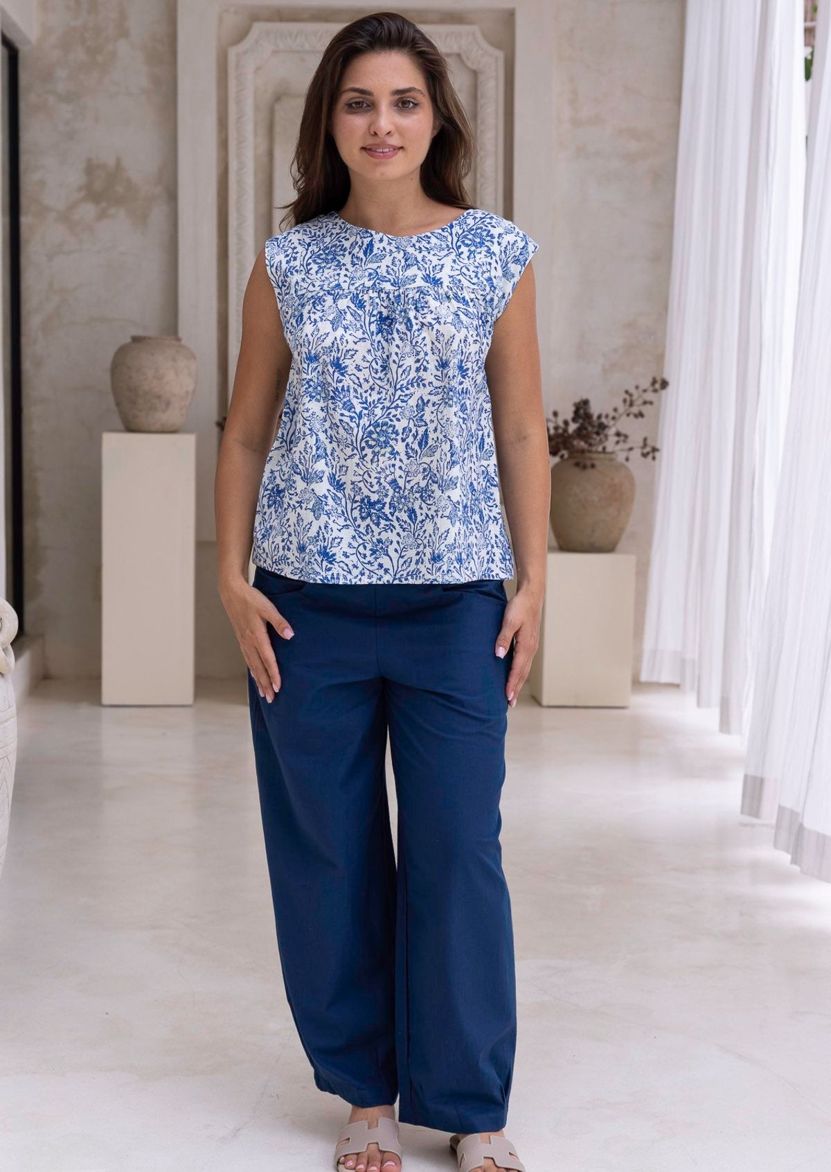 Woman standing in a deep blue wide leg cotton pants with high waste, pockets and pleated ankles 