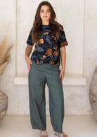 Model wearing 100% cotton green tapered pants with pleats at ankles, pockets and side zipper