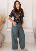 Model posing in a jungle green 100 percent cotton pants, paired with a black floral printed top 