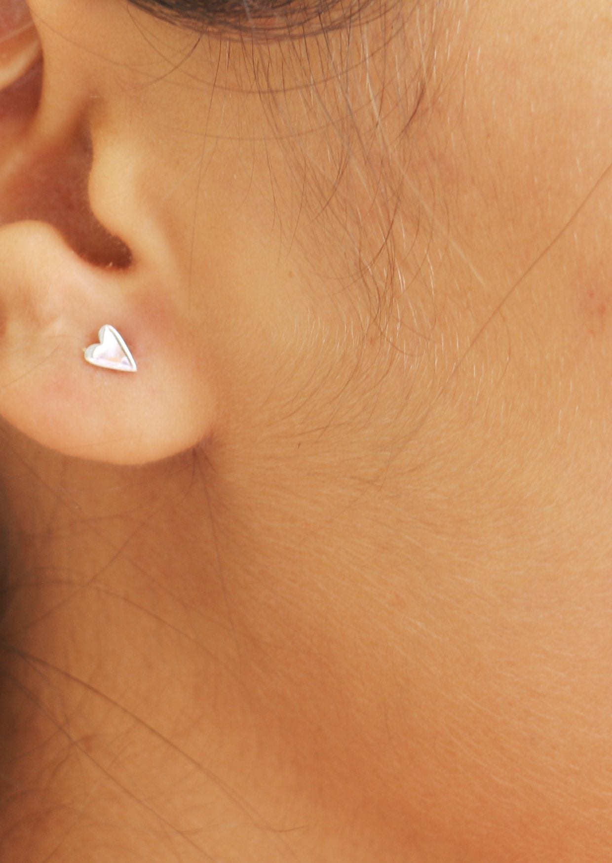 Close-up of an ear wearing elongated heart shaped silver studs