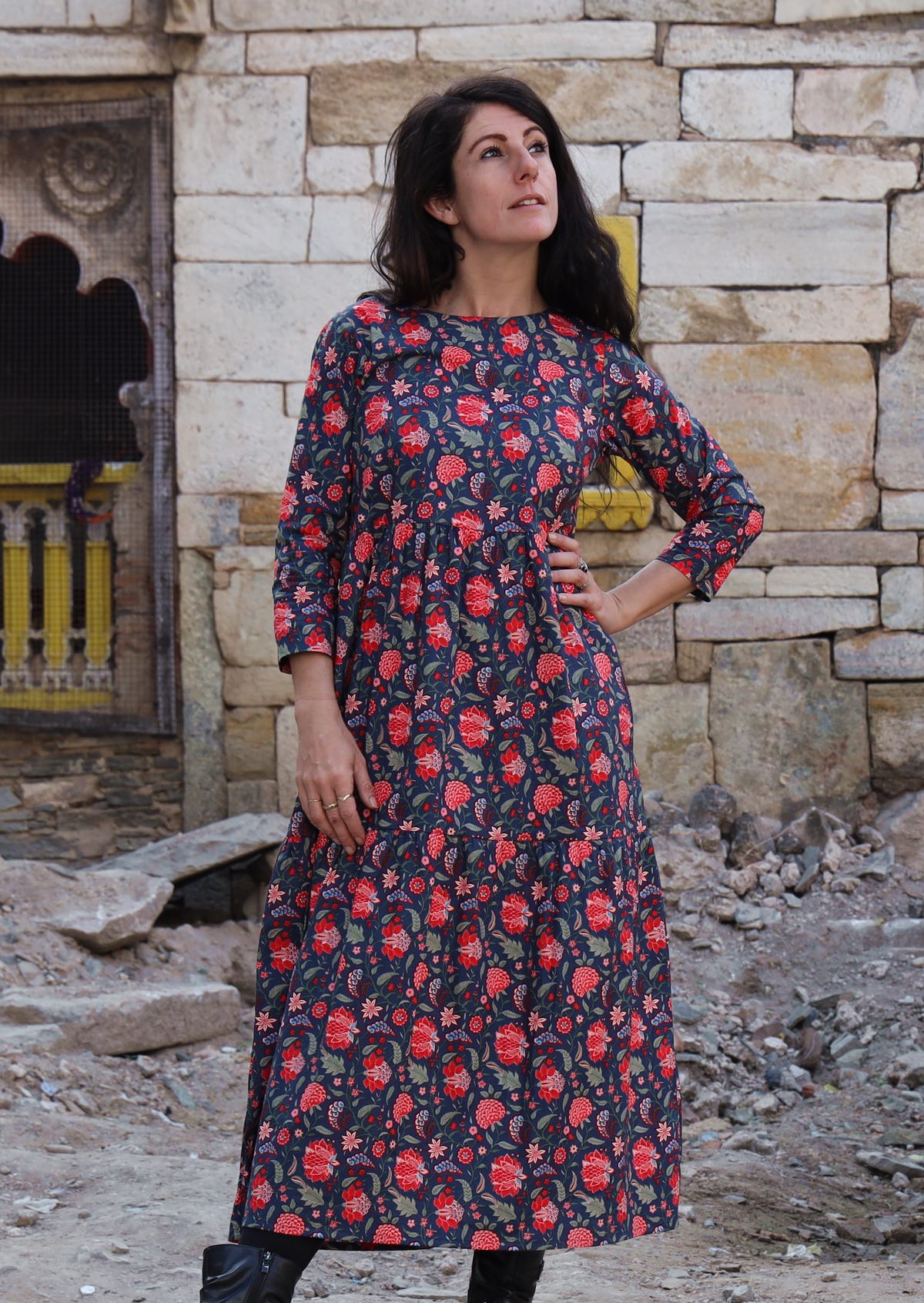 Model standing with hand on hip wearing a 100 percent cotton three tiered midi length dress with blue base and red floral print
