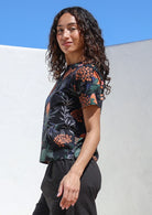 Woman wearing black cotton pants with loose fitting black botanical print cotton top with short sleeves and high round neckline 