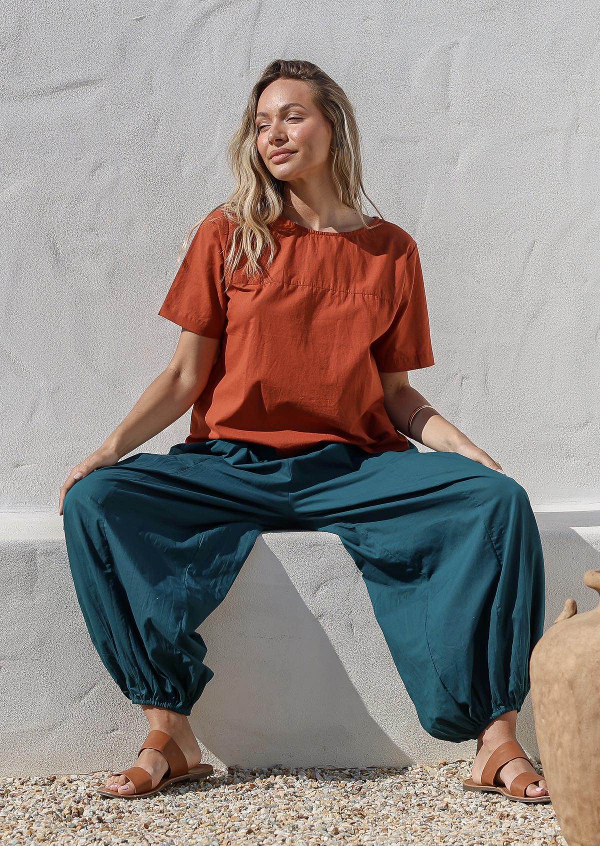 Woman sitting on a concrete block wearing a deep teal 100% cotton harem pants designed in Australia