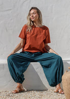 Woman sitting on a concrete block wearing a deep teal 100% cotton harem pants designed in Australia