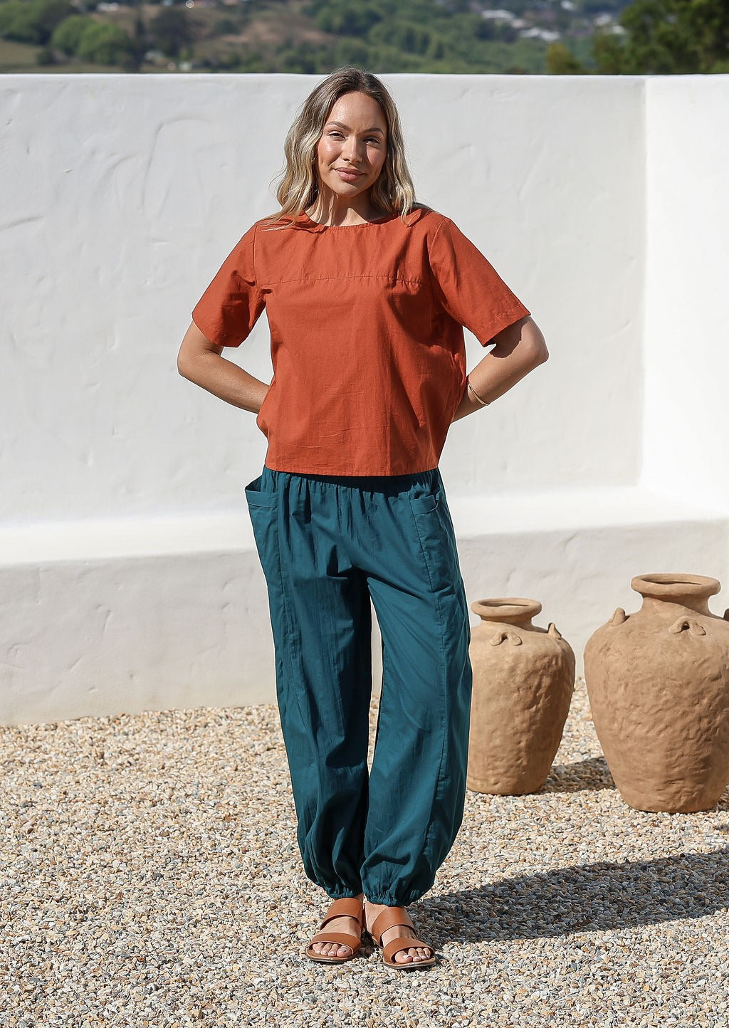 Woman wears wide waistbanded cotton harem pants with a rust short sleeve top 