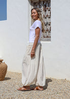 Woman wearing a white t-shirt and white wide-leg cotton pants standing in front of a white wall 