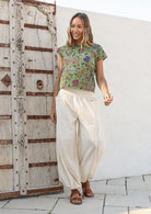Woman wears wide waistbanded cotton harem pants with a green floral top and brown sandals