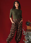 Model wears loose fit 100% cotton pants with pockets, elasticated waist and ankles. A red and olive floral pattern sit on a black base.