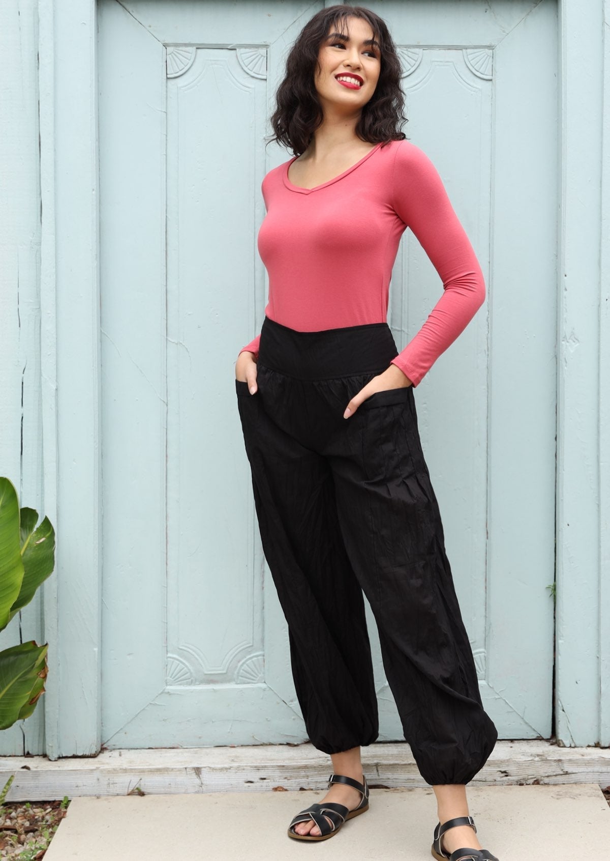 Woman wears relaxed fit lightweight black cotton harem pants with pockets paired with a pink top