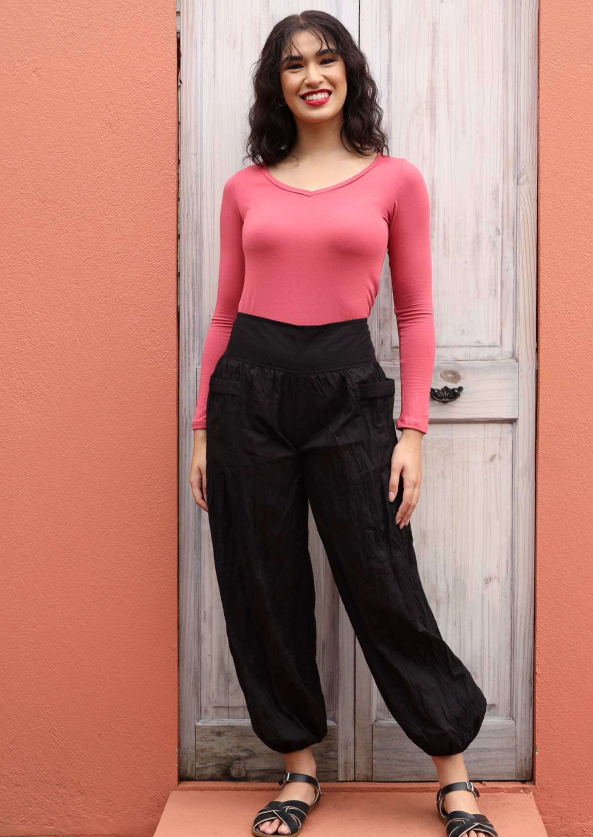 Woman wears wide waistbanded cotton harem pants with a pink long sleeve top and black sandals