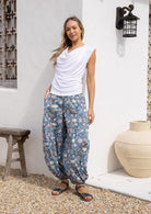 Woman wearing a boho style 100% cotton pants with sweet pink, yellow and green florals on dusty blue base.