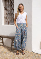 Model standing in sun wearing a relaxed fit, boho cotton pants with lemon yellow, pink and green florals on a blue base.