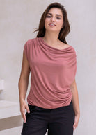 Woman wearing a pink sleeveless top with a draped neckline against a neutral background