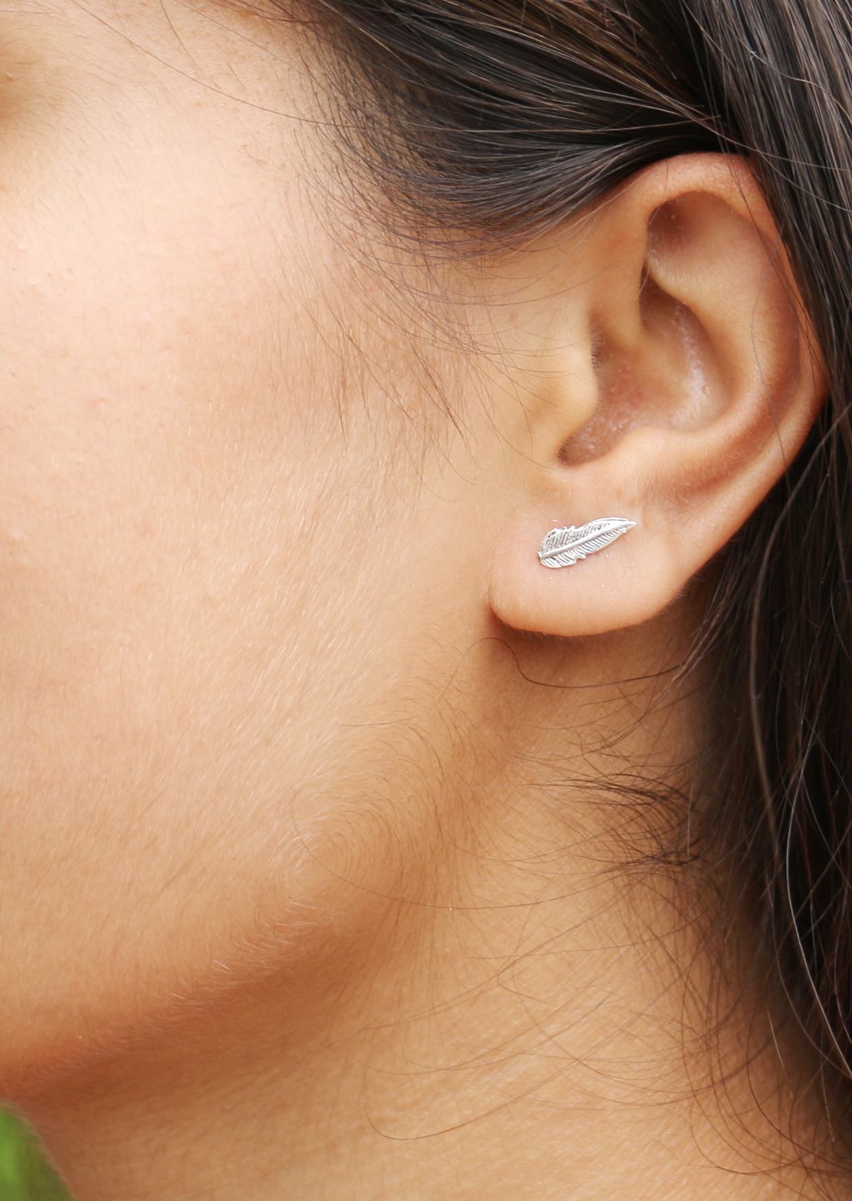 Woman wearing elegant sterling silver plumage studs featuring finely detailed, flowing feather design