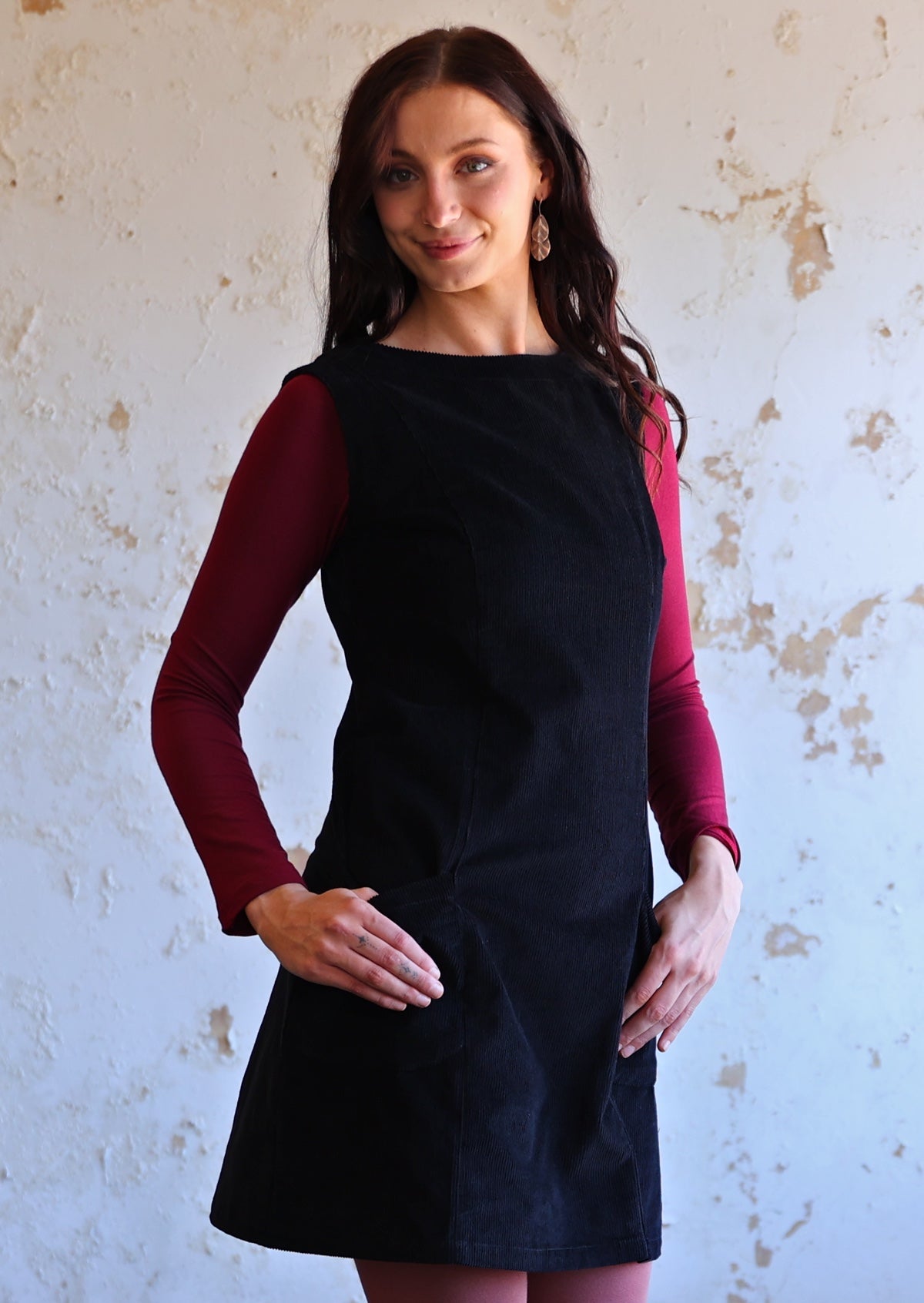 Woman wears cotton corduroy tunic in black with maroon long sleeve top and leggings in underneath