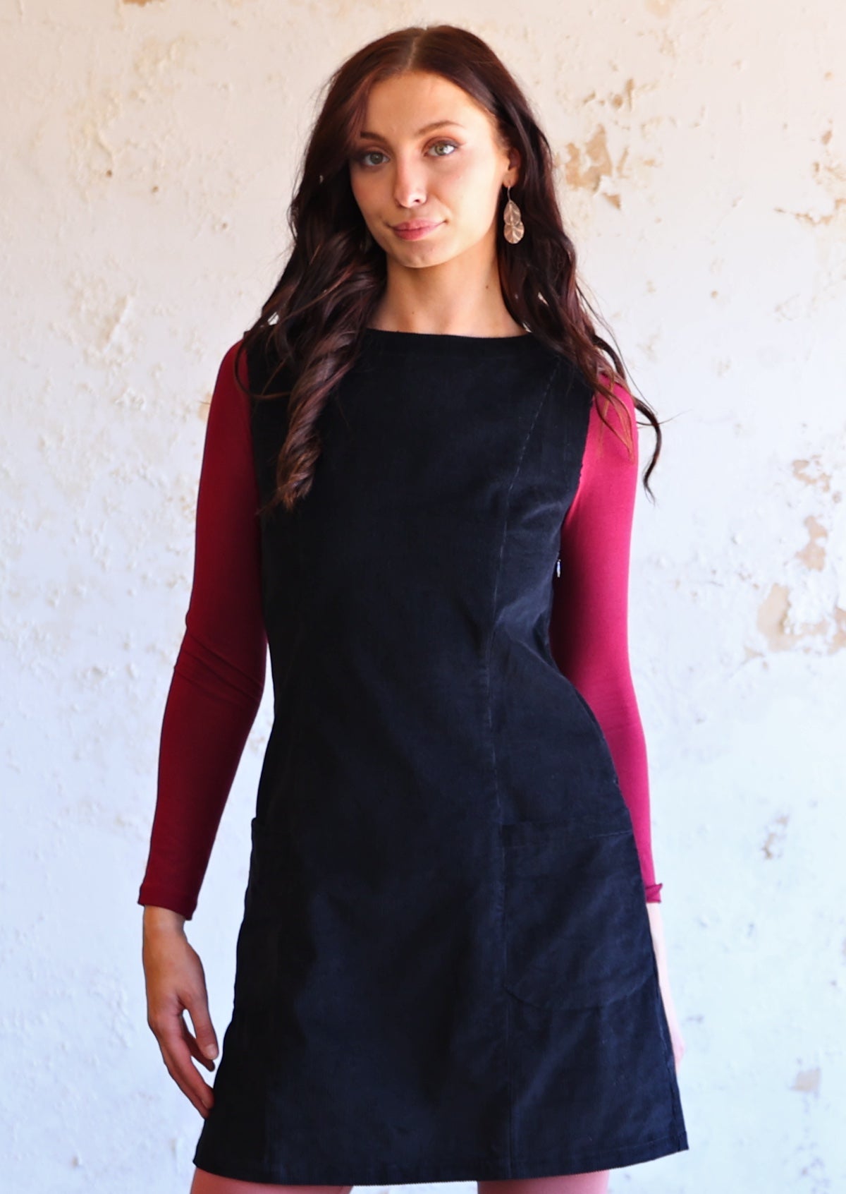 Woman wears cotton corduroy tunic in black with maroon long sleeve top underneath 