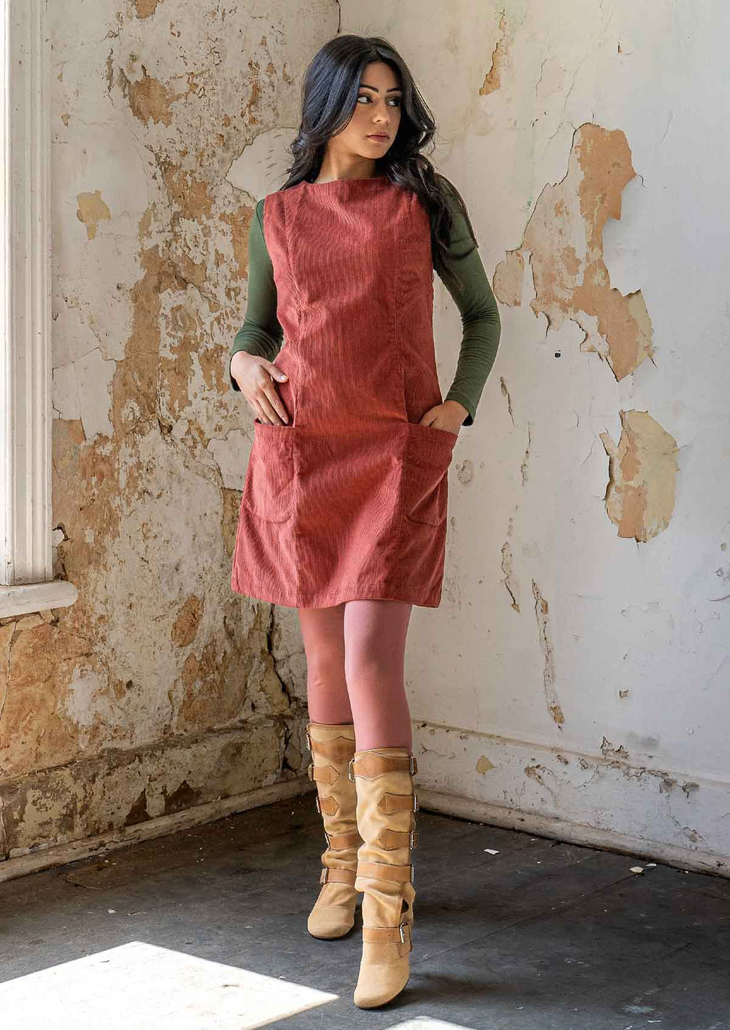 Model wears burnt henna coloured corduroy sleeveless tunic with high round neckline and pockets