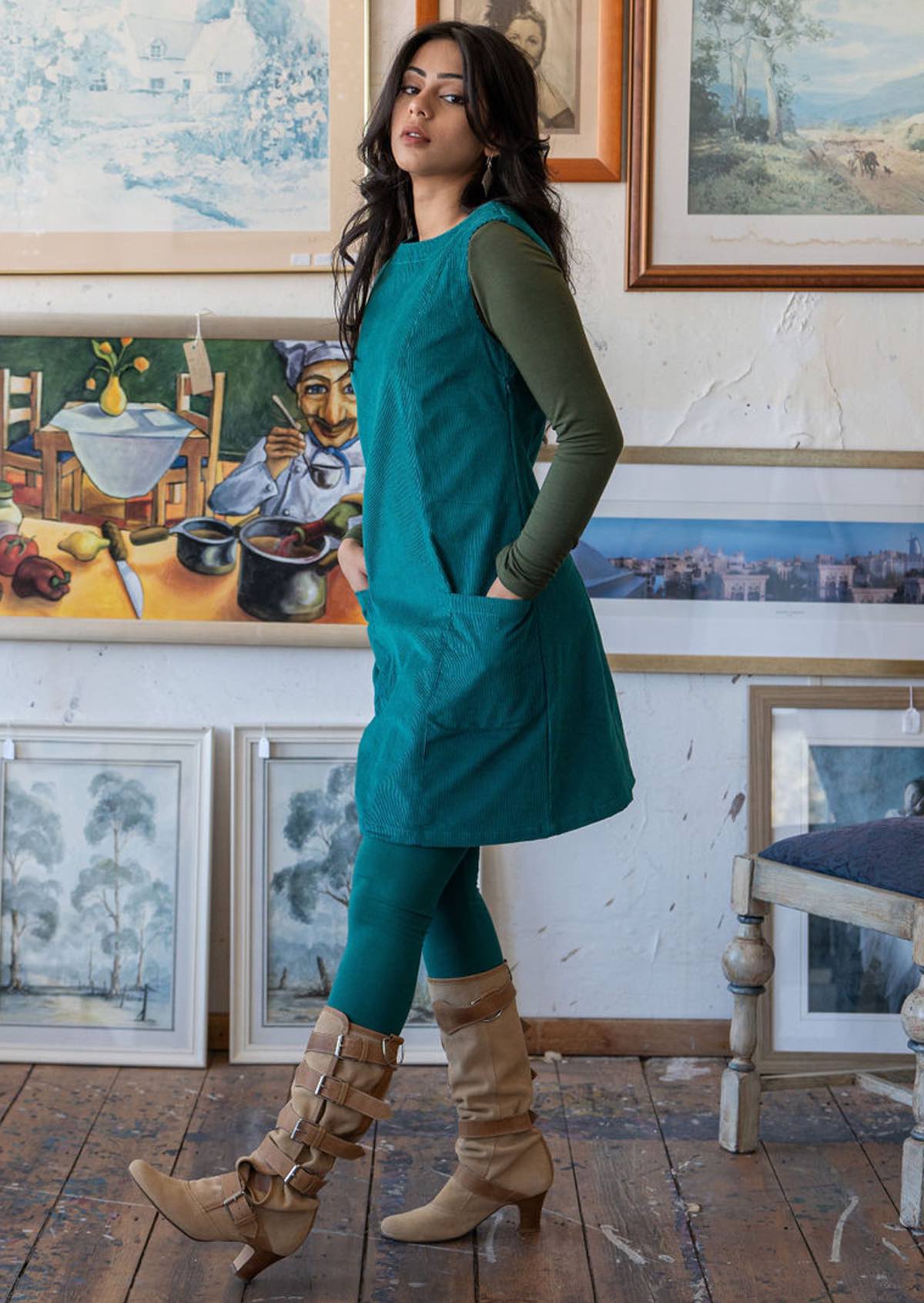 Model stands side on in teal corduroy sleeveless tunic with side zip, high round neckline and pockets