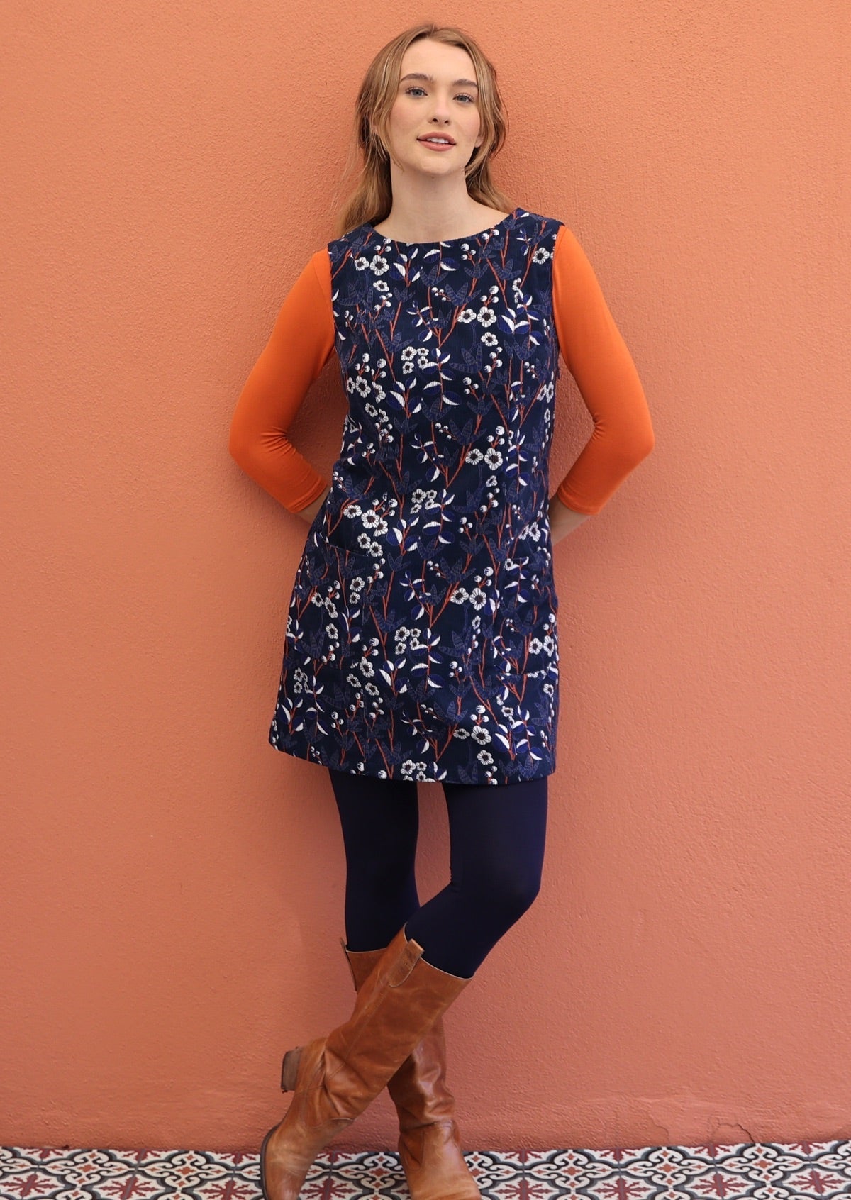 Women standing with her hands back pairs a 100% cotton cord tunic with a long sleeve top, leggings and boots.