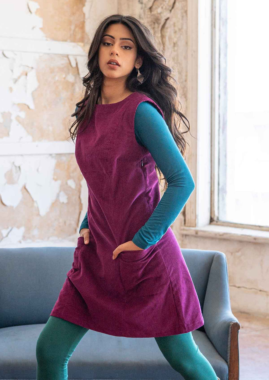 Model strikes a pose in plum purple corduroy tunic that has a high round neckline, a side zip and is sleeveless