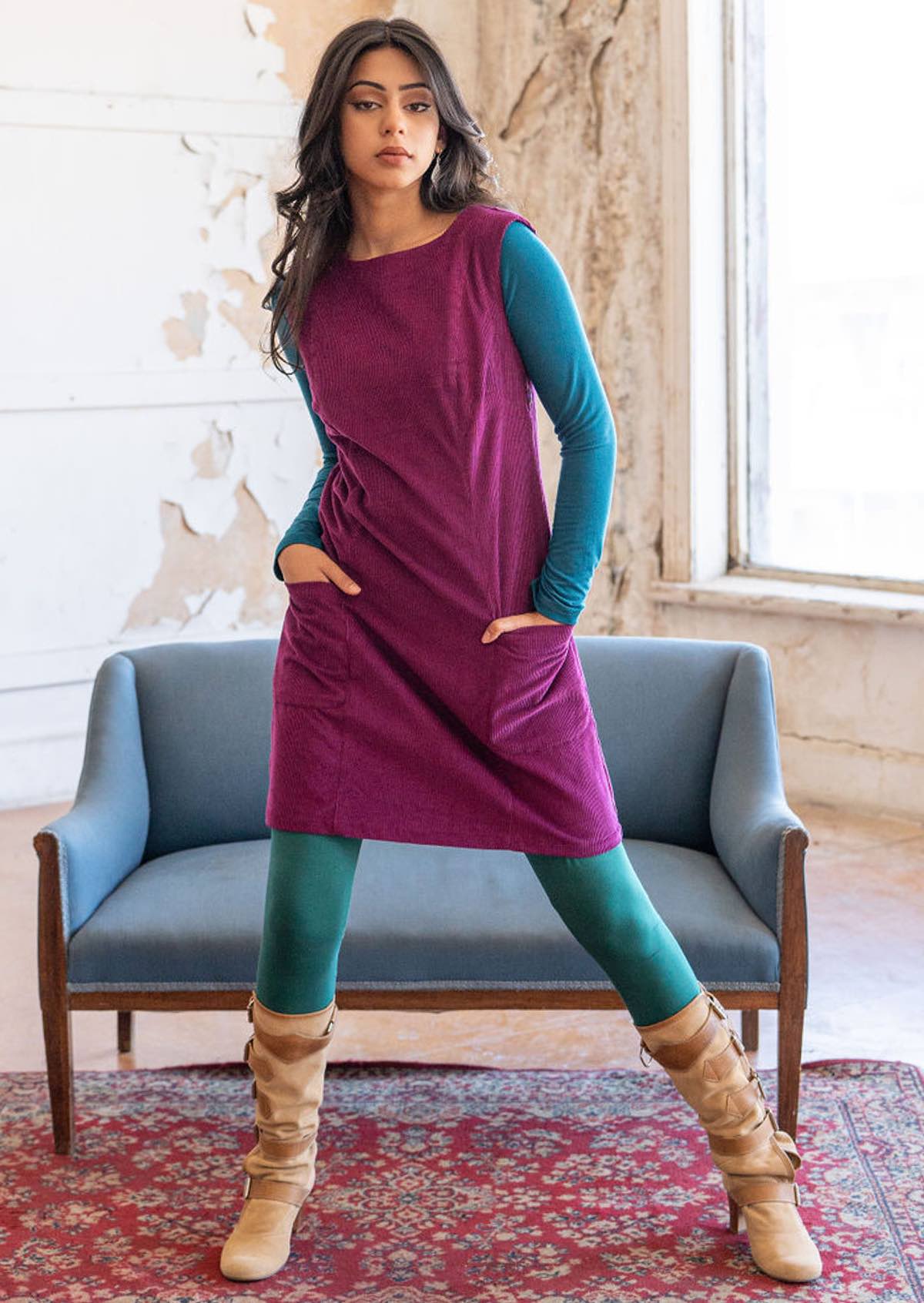 Woman wears bright plum purple corduroy sleeveless tunic with high round neckline and deep pockets