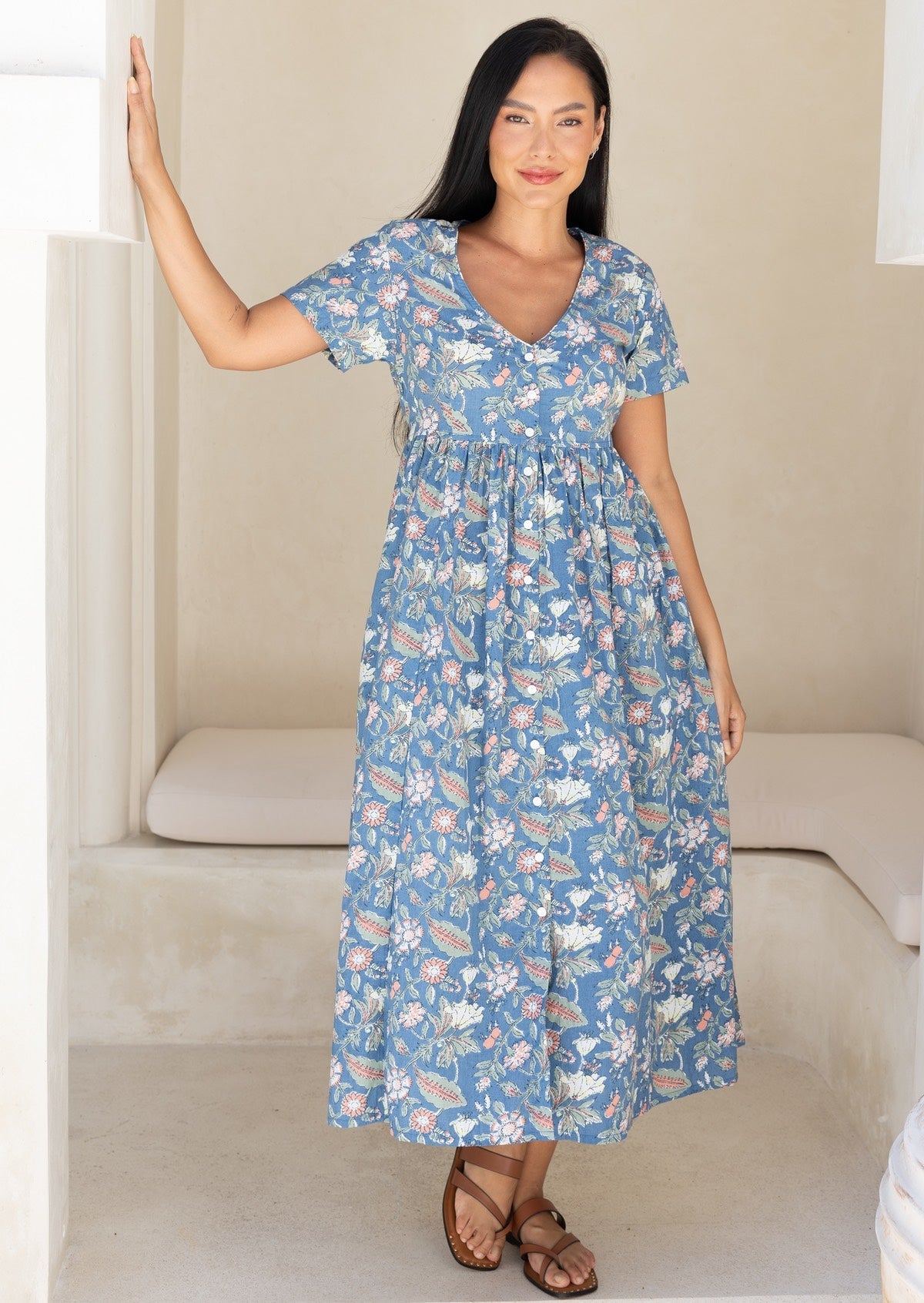 Woman wearing a blue floral cotton midi length relaxed fit dress with short sleeves and a V-neckline and buttons through the centre front