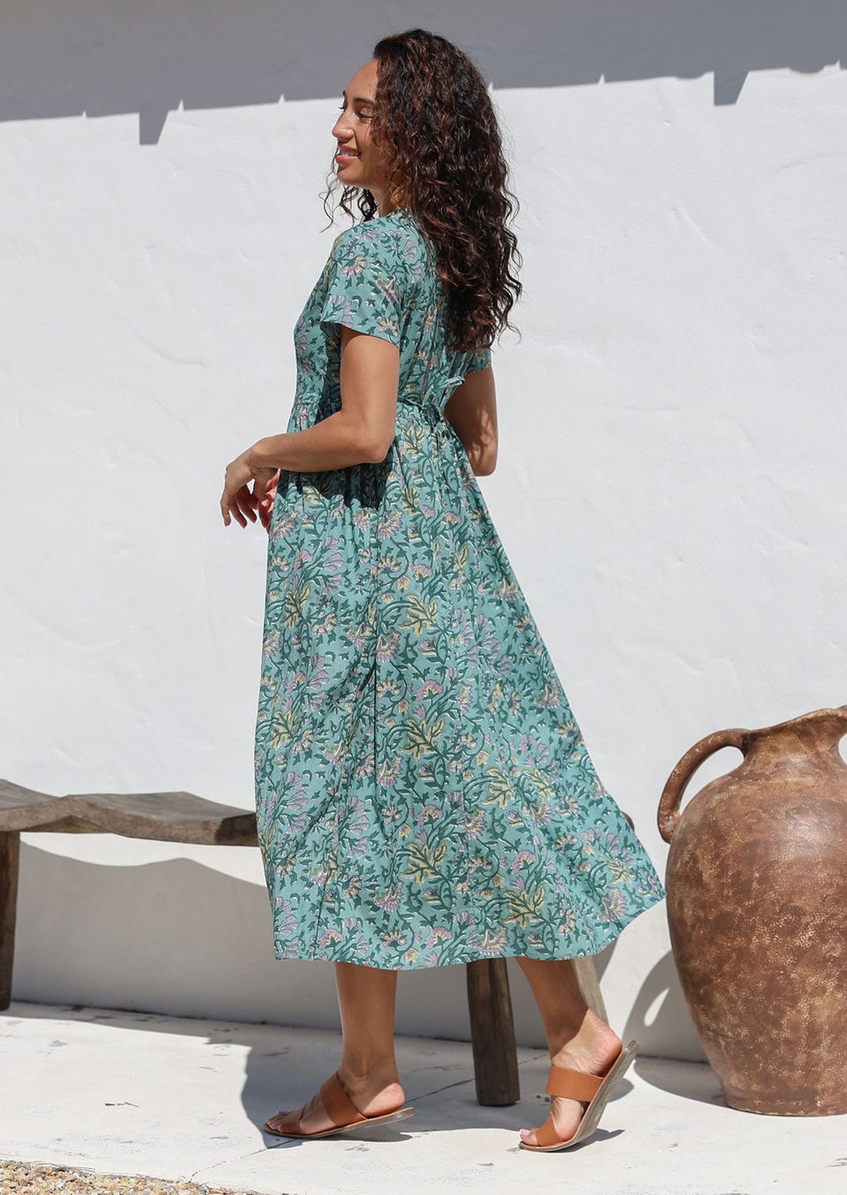 Model poses in 100% cotton sage green floral midlength dress with shoestring tie, side pockets, short sleeves and V neckline