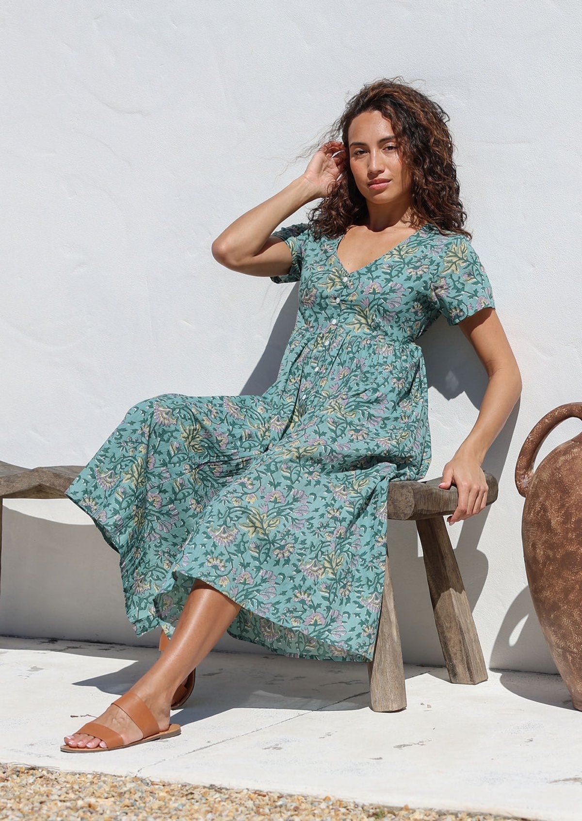 Woman sitting on a wooden bench in sage green floral cotton dress with button front, short sleeves, V neckline and pockets