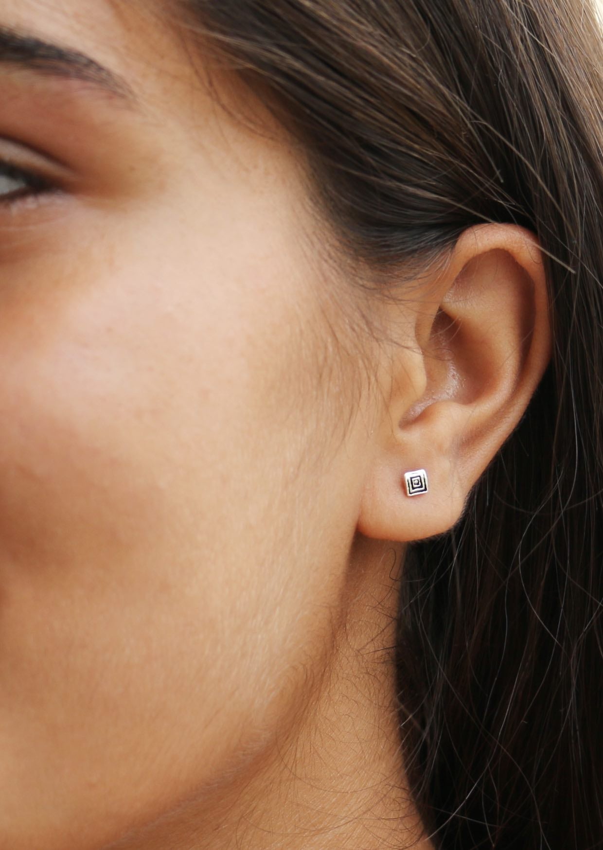 Close-up of an ear wearing a small square shaped studs with polished ripples
